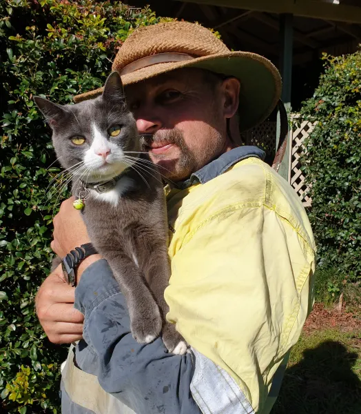 Man in a hi-vis shirt and hat holding a grey and white cat