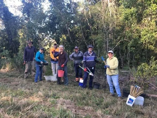 Group of volunteers with buckets, tools and tubestock standing in bushland at a planting day