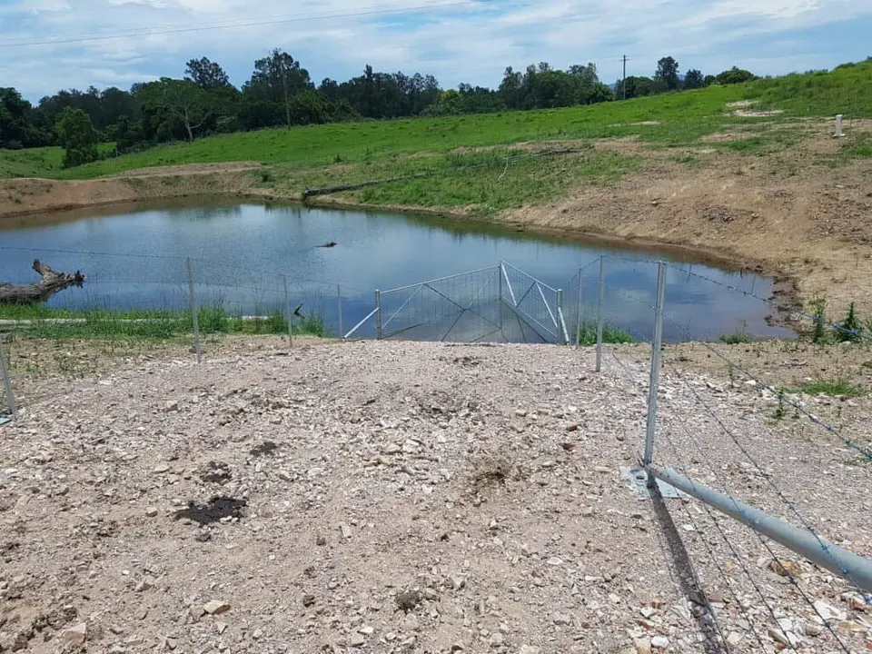 Fenced farm dam with a rocky bank and green pasture beyond, restored for biodiversity