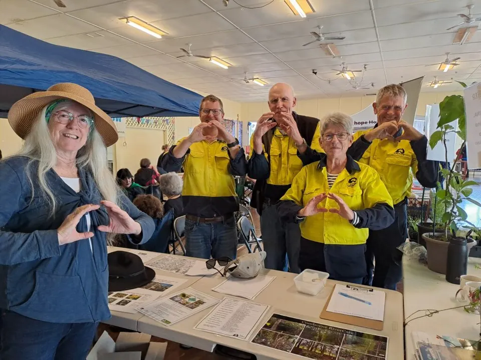 Landcare volunteers making heart shapes with their hands at a community market stall in a hall
