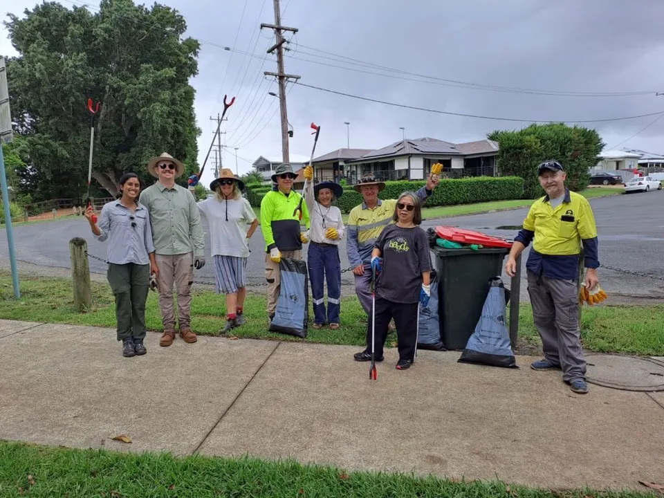 Volunteers in hats and hi-vis holding litter pickers and rubbish bags on a suburban street corner