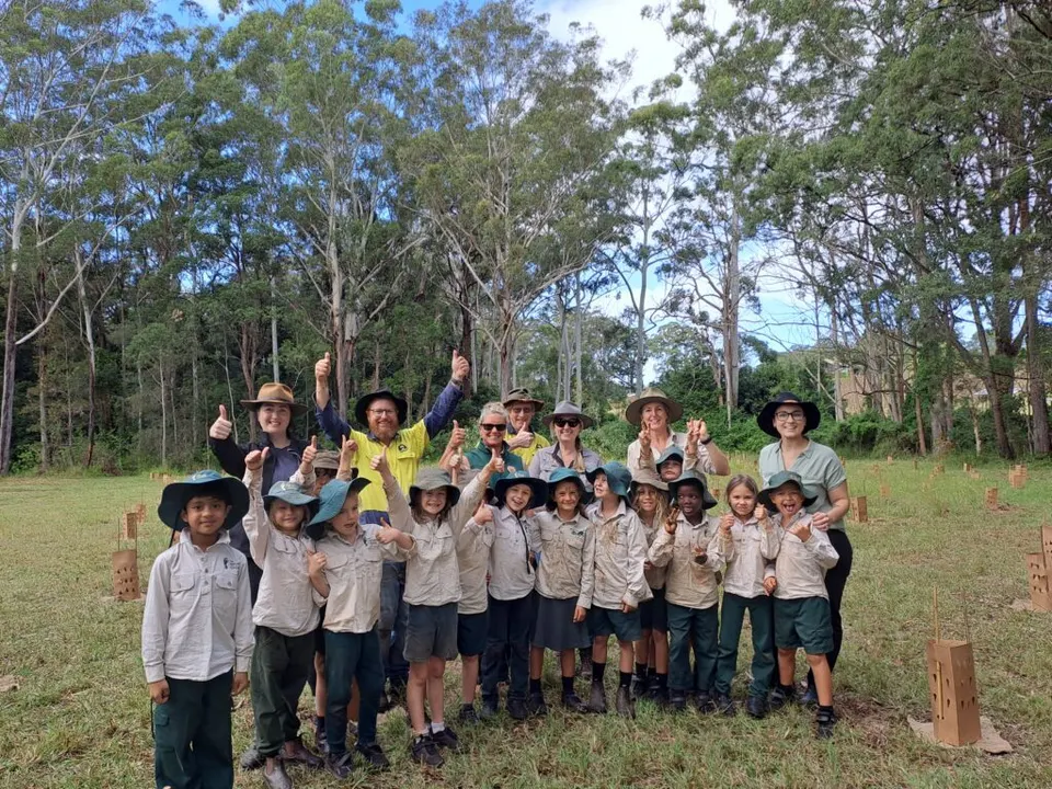 Group of school students in uniforms and bush hats cheering at a planting site with tree guards