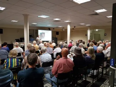 Community members seated in a hall watching a presentation on a projector screen