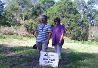 Two landholders standing on a cleared bank beside a Landcare natural resource management sign